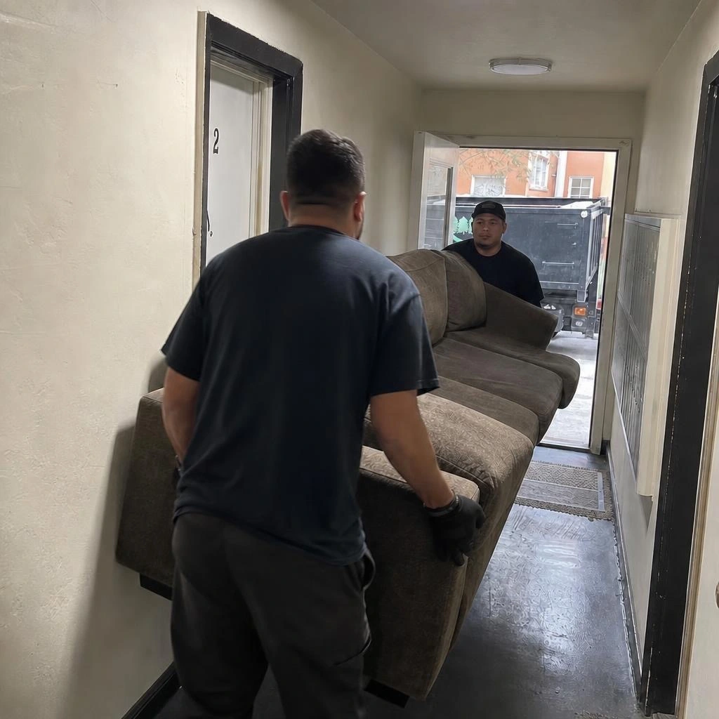 Two-man crew carrying a sectional couch out of an Oakland apartment hallway